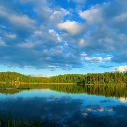 Zdjęcie przedstawia błękitne jezioro w którym odbija się zielony las.
