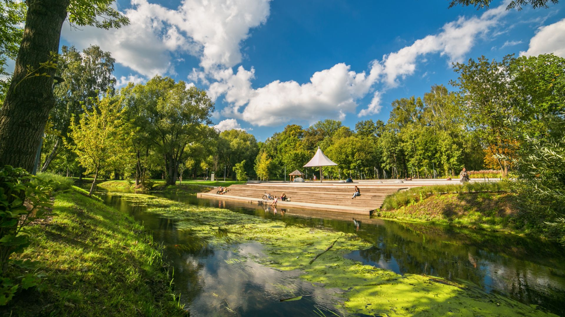 Zdjęcie przedstawia Park Centralny w Olsztynie poprzez który płynie rzeka Łyna.