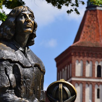 Zdjęcie przedstawia pomnik z brązu Mikołaja Kopernika, który stoi na olsztyńskim starym mieście.