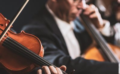 Dwóch muzyków podczas koncertu muzyki klasycznej w galowych garniturach, grających na skrzypcach i kontrabasie.