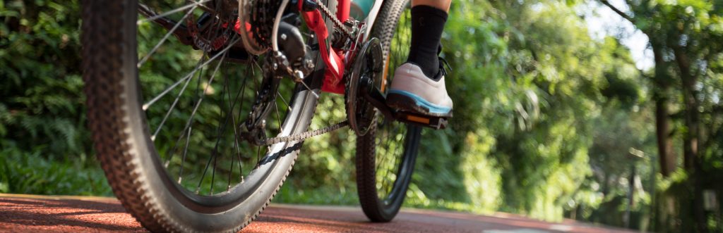 Tył roweru i prawa noga rowerzysty jadącego utwardzoną ścieżką  rowerową w lesie.   