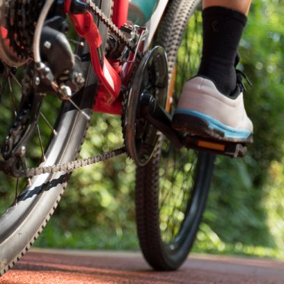 Tył roweru i prawa noga rowerzysty jadącego utwardzoną ścieżką  rowerową w lesie.   