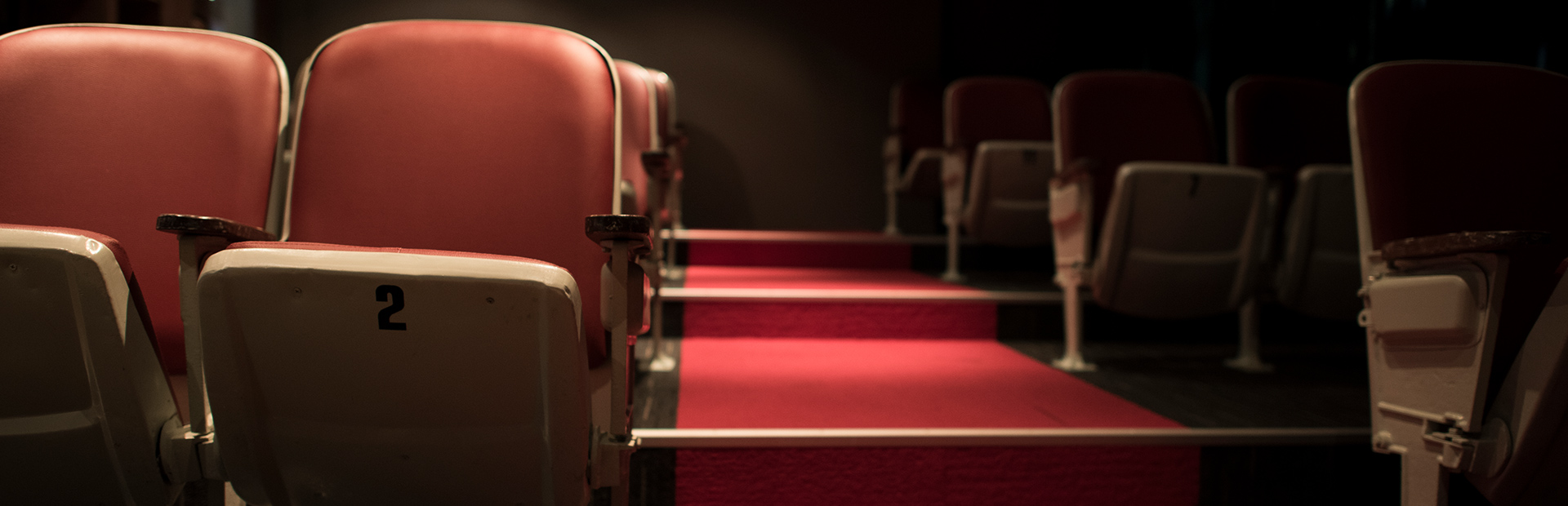 Rząd krzeseł na widowni w teatrze, a obok przejście pomiędzy rzędami krzeseł.     