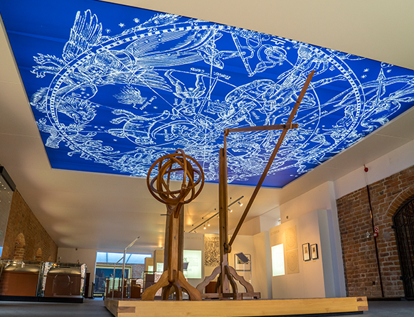 Zdjęcie przedstawia wnętrze sali z niebieskobiałym sufitem będącym częścią Muzeum Mikołaja Kopernika we Fromborku.