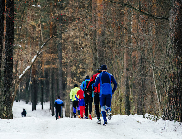 Zawodnicy biegnący gęsiego zimą po śnieżnej ścieżce leśnej.  