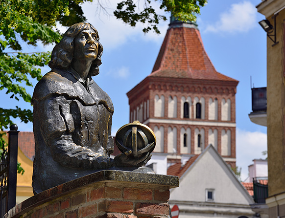 Zdjęcie przedstawia pomnik z brązu Mikołaja Kopernika, który stoi na olsztyńskim starym mieście.