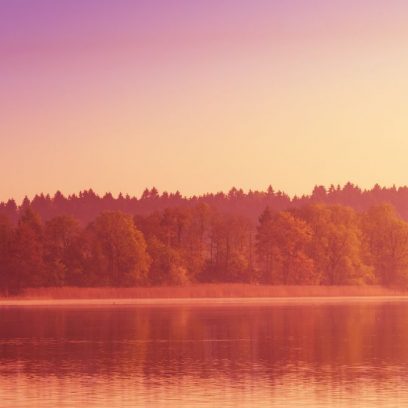 Zdjęcie przedstawia dwie łódki bez załogi dryfujące na jeziorze w czasie zachodu słońca chowającego się za linią drzew.