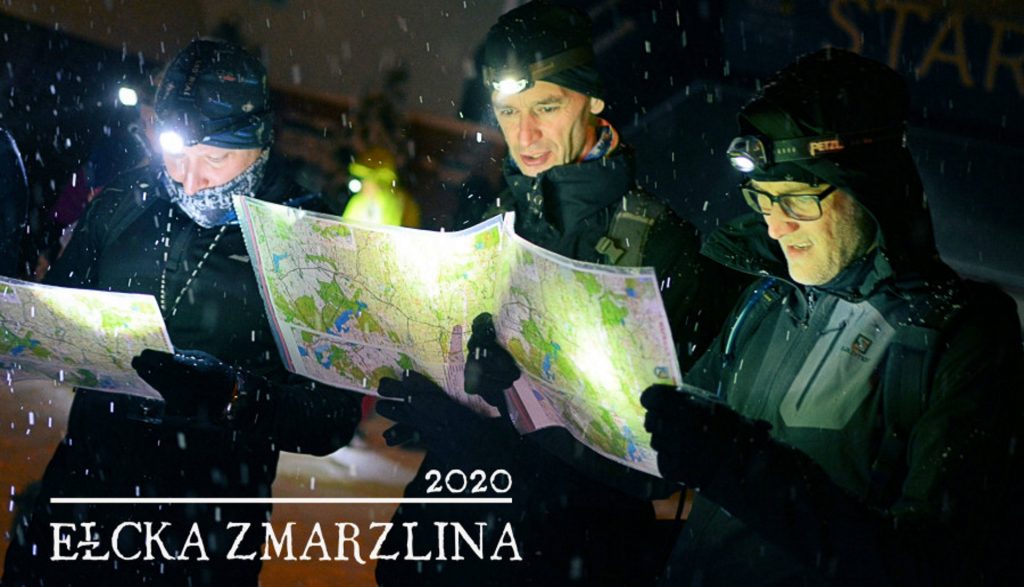 Zdjęcie przedstawia zawodników uczestniczących w zawodach, studiujących mapę zawodów.   