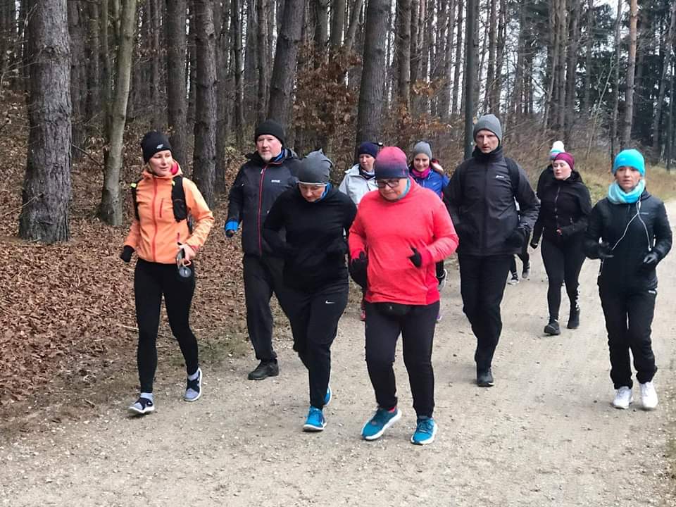 Zdjęcie przedstawiające biegaczy podczas rozgrzewki truchtających ścieżką wśród lasów olsztyńskich.   