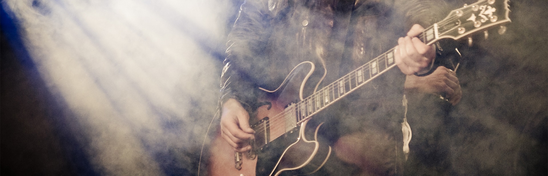Muzyk podczas koncertu grający na gitarze, w smudze reflektorów i scenicznego sztucznego dymu.    
