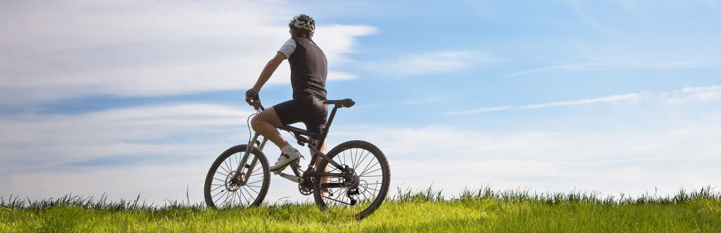 Stojący samotny rowerzysta na mazurskim polu, wśród bujnej zielonej trawy.   