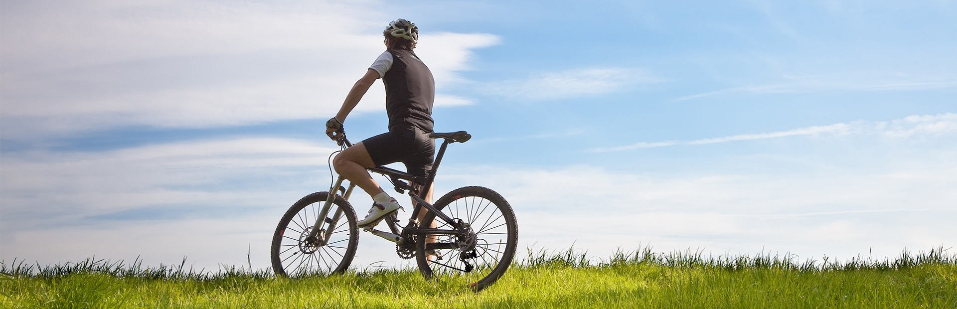 Stojący samotny rowerzysta na mazurskim polu, wśród bujnej zielonej trawy.   