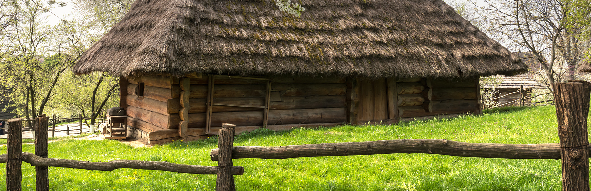 Stara drewniana chata mazurska pokryta słomą a wokół domu rosnąca zielona trawa.  