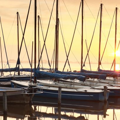 Przycumowane stojące w szeregu żaglówki na mazurskim jeziorze
w podczas wschodu słońca.   