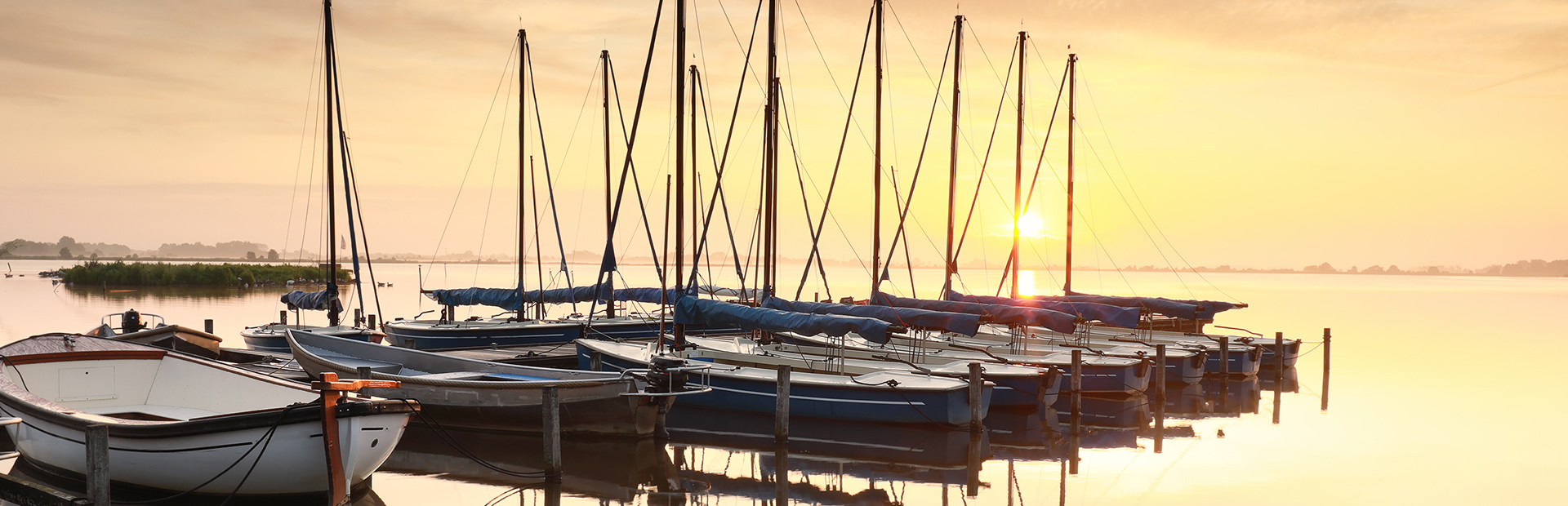 Przycumowane stojące w szeregu żaglówki na mazurskim jeziorze
w podczas wschodu słońca.   