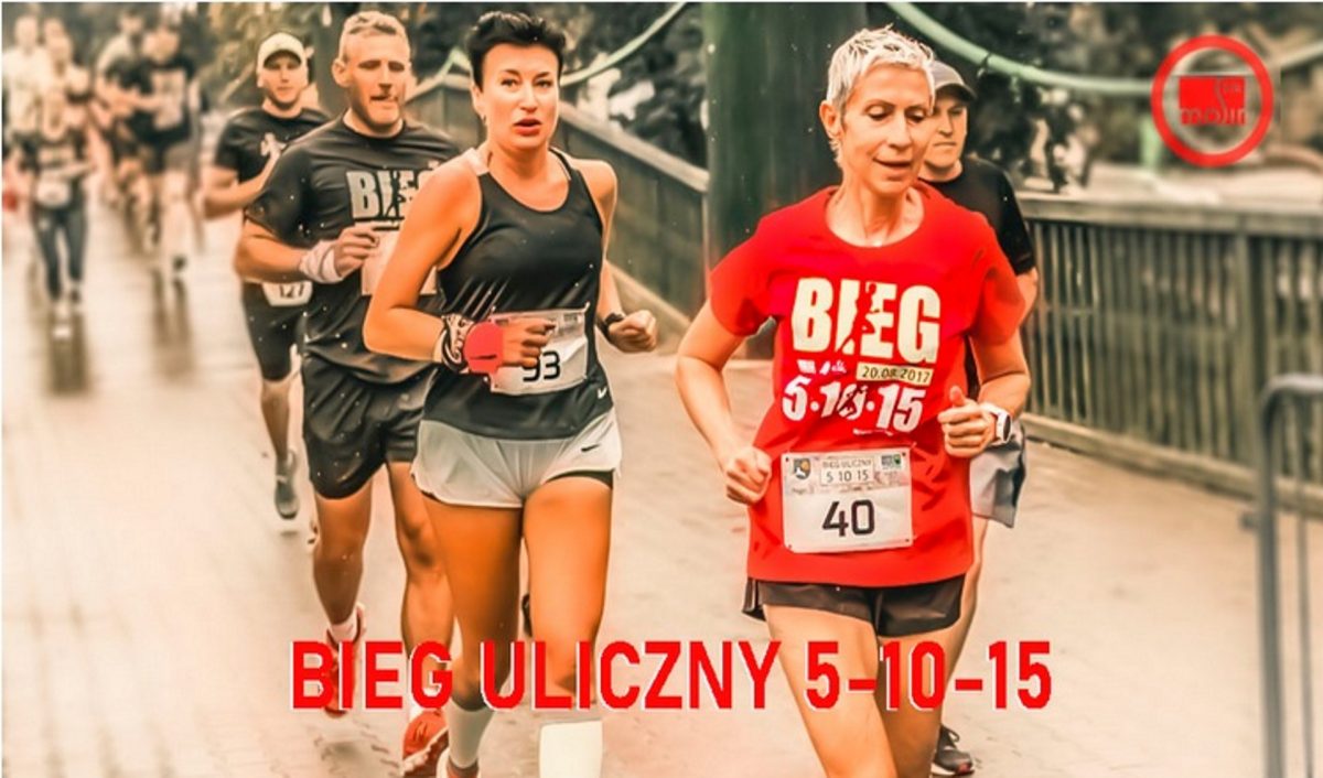 Zdjęcie przedstawia biegaczy podczas zawodów biegu ulicznego 5-15-15 w Ełku. Na zdjęciu pięciu zawodników dwie kobiety i trzech mężczyzn biegnących po ulicach miasta. 