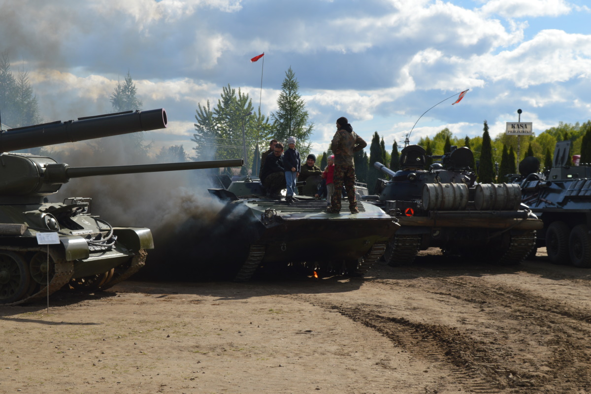 Na zdjęciu czołgi z Mrągowskiego Muzeum Sprzętu Wojskowego poustawiane w rzędzie. Na czołgach turyści z dziećmi zwiedzający sprzęt wojskowy. 