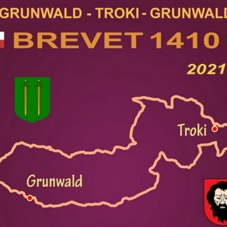 Plakat zapraszający do udziału w zawodach Ultra Maraton Kolarski Grunwald-Troki-Grunwald 1410 km - 2021. Plakat graficzny posiadający fioletowe tło na którym narysowany jest kontur mapy trasy zawodów i napisy o imprezie.    