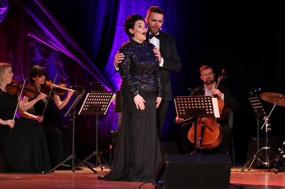 Zdjęcie zapraszające do Giżycka na 6. edycję Mazurskiego Festiwalu Operowego BELCANTO Giżycko – 2021. Na zdjęciu para śpiewaków operowych podczas koncertu.