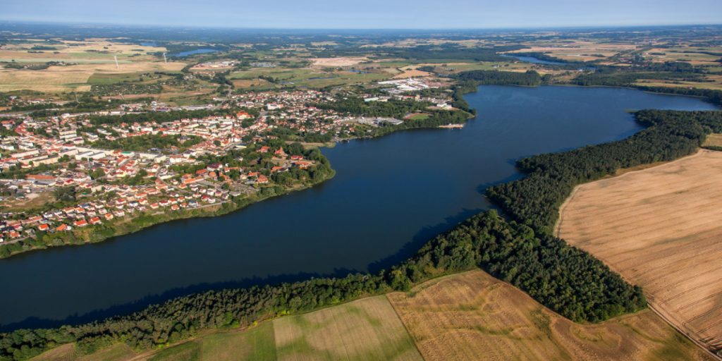 Panorama miasta Olecka. Na zdjęciu widzimy miasto z lotu ptaka oraz jezioro i okalające łąki i pola uprawne.    