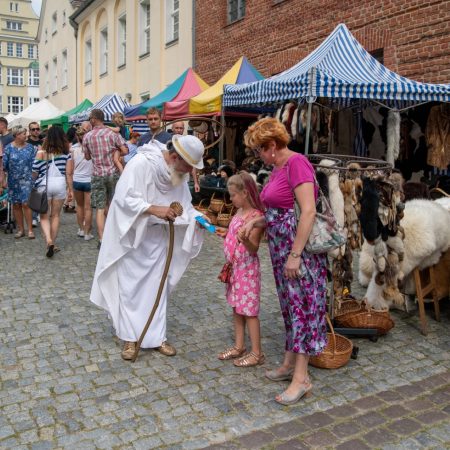 Zdjęcie wykonane podczas odbywającego się w latach poprzednich Jarmarku Jakubowego na Starym Mieście w Olsztynie. Na zdjęciu widzimy spacerujących turystów i mieszkańców Olsztyna pomiędzy straganami.