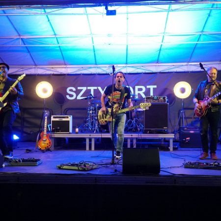 Zdjęcie z koncertu szantowego, który odbył się w porcie Sztynort. Na zdjęciu widzimy zespół na scenie podczas występu.  