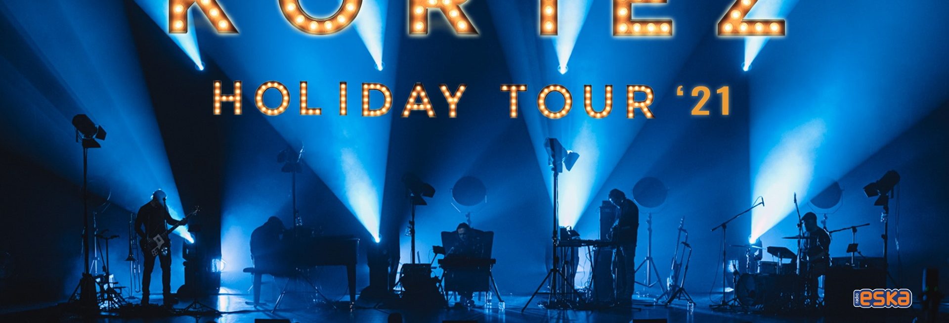 Plakat graficzny zapraszający do Ostródy na koncert Kortez Holiday Tour - Ostróda 2021. Na plakacie scena koncertowa na której występuje Kortez i jego zespół. 