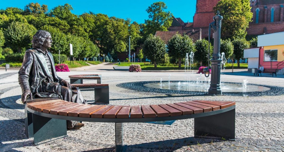 Zdjęcie przedstawia rzeźbę Mikołaja Kopernika na ławeczce, zlokalizowaną w parku we Fromborku.     